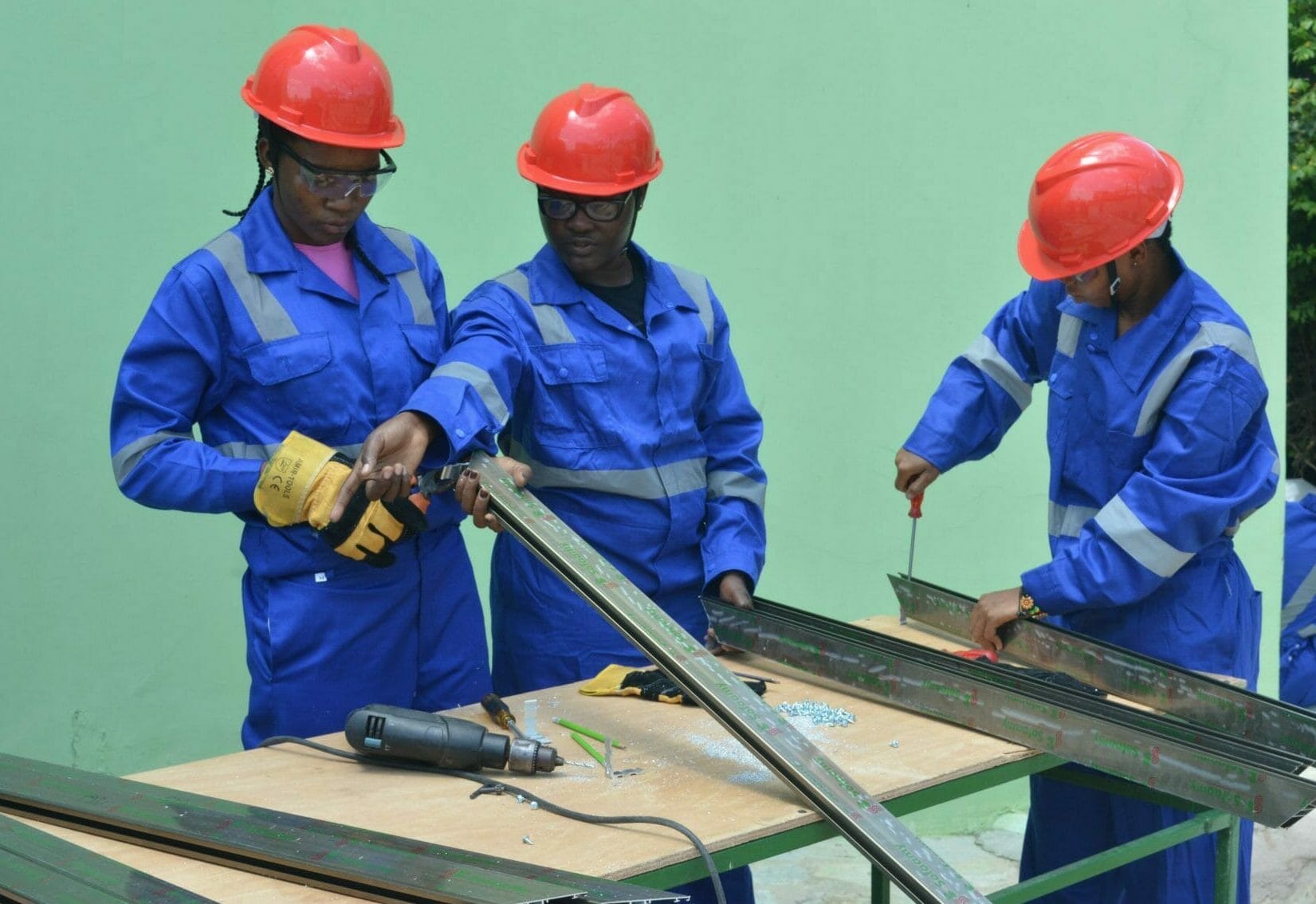 Three Ghanaian construction workers work with steel beams.